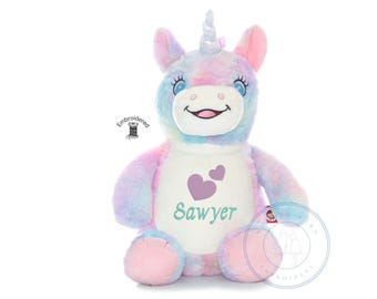 May include: A plush unicorn toy with pastel tie-dye fur in shades of pink, blue, and purple. The unicorn features a silver horn, a white muzzle, and a white belly patch embroidered with two purple hearts and the name Sawyer in teal script.