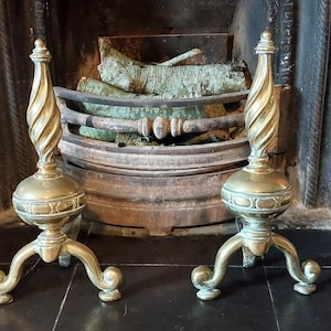 May include: A pair of antique brass fire irons with a spiral design on the top. The fire irons are sitting in front of a fireplace.
