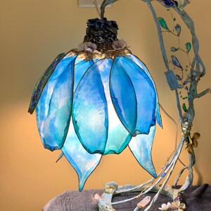 May include: A blue and white lamp with a unique design. The lampshade is made of fabric and has a flower-like shape. The base of the lamp is made of twisted branches and decorated with crystals and beads.