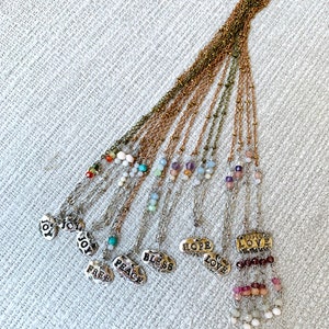 Puede incluir: Un conjunto de 12 collares de plata con diferentes cuentas de piedras preciosas y dijes. Cada dije presenta una palabra diferente, incluyendo "Alegr&iacute;a", "Paz", "Bendici&oacute;n", "Esperanza", "Amor" y "Libre".