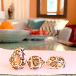 May include: Three white rings with gold and pink accents. The rings are decorated with small, colorful stones and glitter.