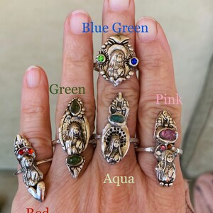K&ouml;nnte beinhalten: F&uuml;nf Silberringe mit verschiedenen farbigen Steinen. Die Ringe zeigen eine religi&ouml;se Figur in der Mitte. Die Steine sind rot, gr&uuml;n, blau, rosa und aquamarin.