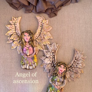 May include: Two ceramic angels with wings made of leaves, holding candles. The angel on the left is labeled "Angel of ascension" and the angel on the right is labeled "Angel of light".