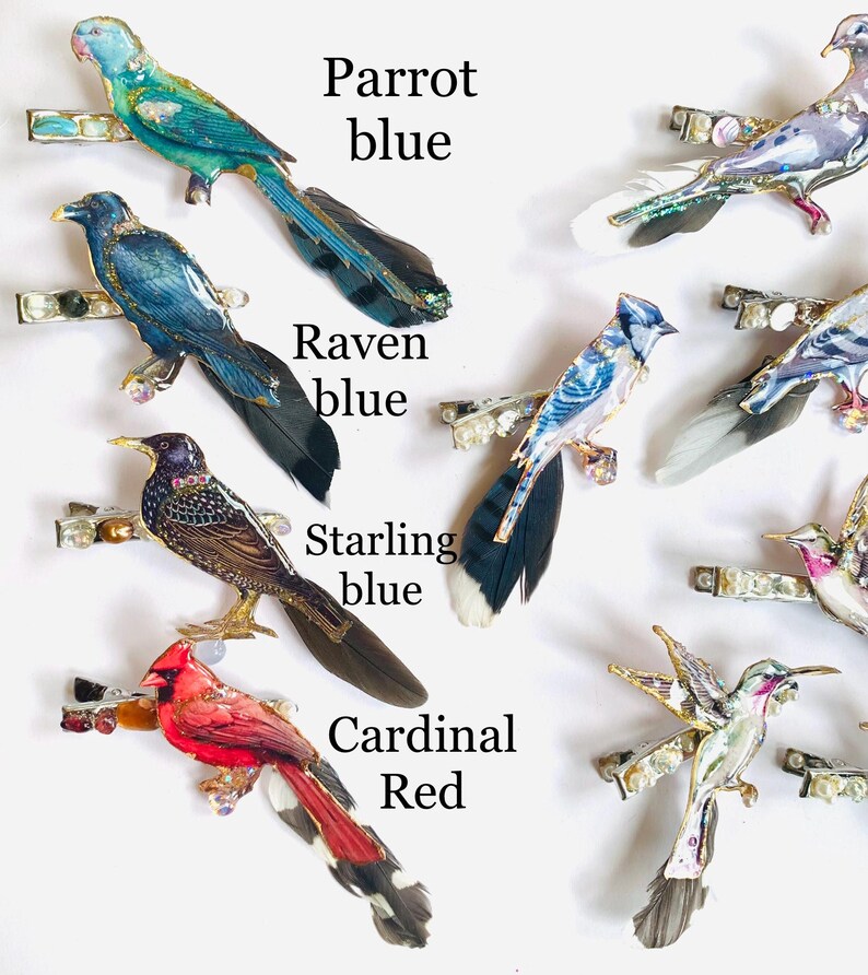 May include: A collection of bird-shaped hair clips featuring a blue parrot, blue raven, blue starling, and red cardinal, each accented with feathers, beads, and metallic details. The text labels Parrot blue, Raven blue, Starling blue, and Cardinal Red appear.