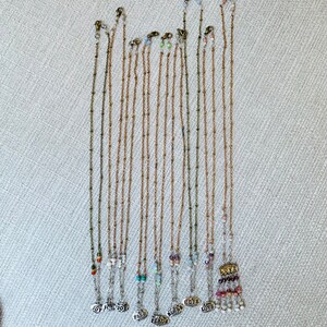 Puede incluir: Una colecci&oacute;n de 12 collares de cadena dorada con cuentas y dijes de varios colores. Cada dije tiene una palabra diferente, incluyendo "Alegr&iacute;a", "Paz", "Amor" y "Esperanza".