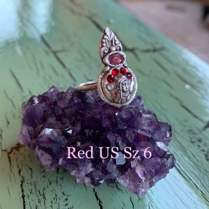 K&ouml;nnte beinhalten: Ein silberner Ring mit einem roten Stein und einem detaillierten Design. Der Ring liegt auf einem Bett aus Amethystkristallen. Gr&ouml;sse 6 US.