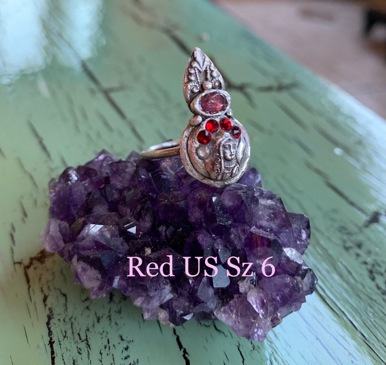 K&ouml;nnte beinhalten: Ein silberner Ring mit einem roten Stein und einem detaillierten Design. Der Ring liegt auf einem Bett aus Amethystkristallen. Gr&ouml;sse 6 US.