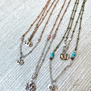 Puede incluir: Cuatro collares de plata con diferentes dijes. Los dijes dicen "Let Go", "Let God" y "Let" con un peque&ntilde;o dije de cuentas. Los collares est&aacute;n sobre un fondo de tela blanca.