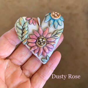 Puede incluir: Un adorno de cer&aacute;mica en forma de coraz&oacute;n con fondo blanco y dise&ntilde;os florales. Las flores son rosas, azules y verdes con detalles dorados. El texto "Dusty Rose" est&aacute; escrito debajo del adorno.