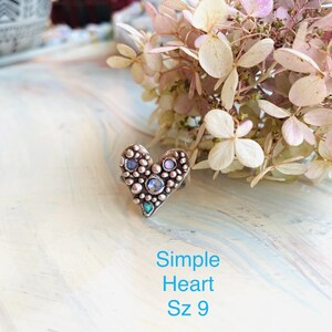 May include: A heart-shaped ring with a textured surface, decorated with small, round embellishments and several iridescent stones. The ring is size 9. The text "Simple Heart Sz 9" is displayed in blue below the ring.