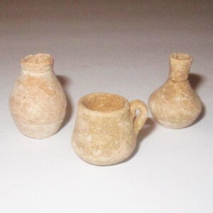 May include: Three small, unglazed, terracotta pottery pieces. Two are round and one is a mug with a handle.