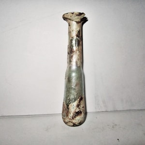 May include: A tall, slender glass bottle with a flared, uneven rim. The glass features a weathered, iridescent surface with mottled patches of brown, white, and translucent green, giving it an aged, textured appearance throughout.