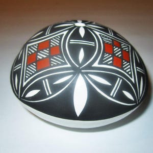 May include: A black and white ceramic pot with red geometric designs. The pot is round and has a smooth surface.