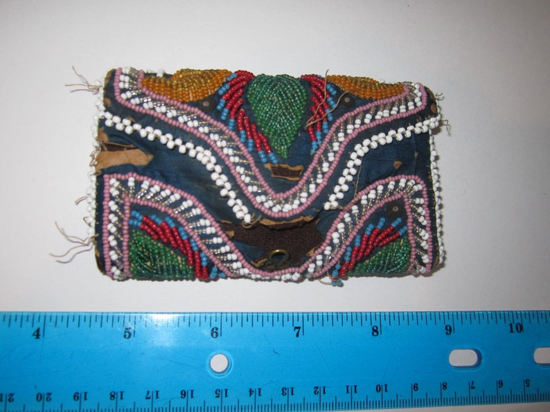 May include: A small, blue fabric pouch with a flap closure, decorated with colorful beads in a geometric pattern. The pouch is approximately 7 inches long and 4 inches wide.