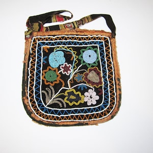 Könnte beinhalten: Eine kleine, geperlte Tasche mit einem Blumendesign in Blautönen, Grün, Rot und Weiß. Die Tasche hat einen braunen Lederriemen und ist aus dunklem Stoff gefertigt.