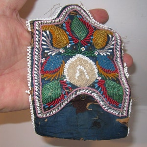 May include: A small, beaded pouch with a blue background and colorful floral designs. The pouch is trimmed with white beads and has a flap closure.