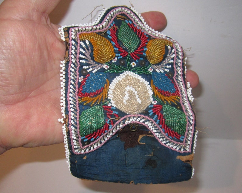 May include: A small, beaded pouch with a blue background and colorful floral designs. The pouch is trimmed with white beads and has a flap closure.