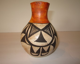 May include: A small, round, white ceramic vase with black and orange geometric designs. The vase has a narrow neck and a wide base.