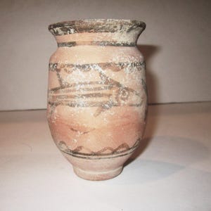 May include: A small, brown clay pot with black painted designs of fish. The pot has a rounded body and a slightly flared rim.