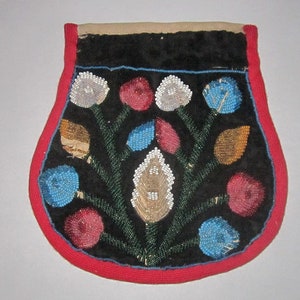Puede incluir: Una bolsa de cuentas con fondo negro y un diseño floral. Las flores son blancas, azules y rojas, y las hojas son verdes. La bolsa está adornada con cuentas rojas y azules.