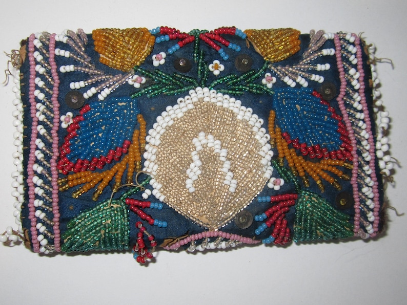 May include: A small, rectangular beaded pouch with a blue background. The pouch is decorated with colorful beads in a floral pattern. The pouch is trimmed with white beads.