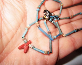May include: A vintage necklace with blue, red, and multicolored beads. The necklace features a silver clasp and a red pendant. The beads are cylindrical and strung together, creating a unique and artistic design. The necklace is displayed on a hand.