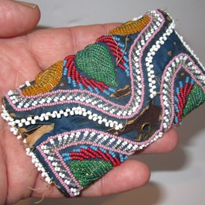 May include: A small, blue fabric pouch with a flap closure, decorated with colorful beads in a geometric pattern. The pouch has a metal clasp and is hand-stitched.