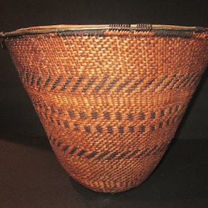 Puede incluir: Una cesta grande, tejida en marrón con un patrón geométrico negro. La cesta tiene forma de cono y una abertura ancha.