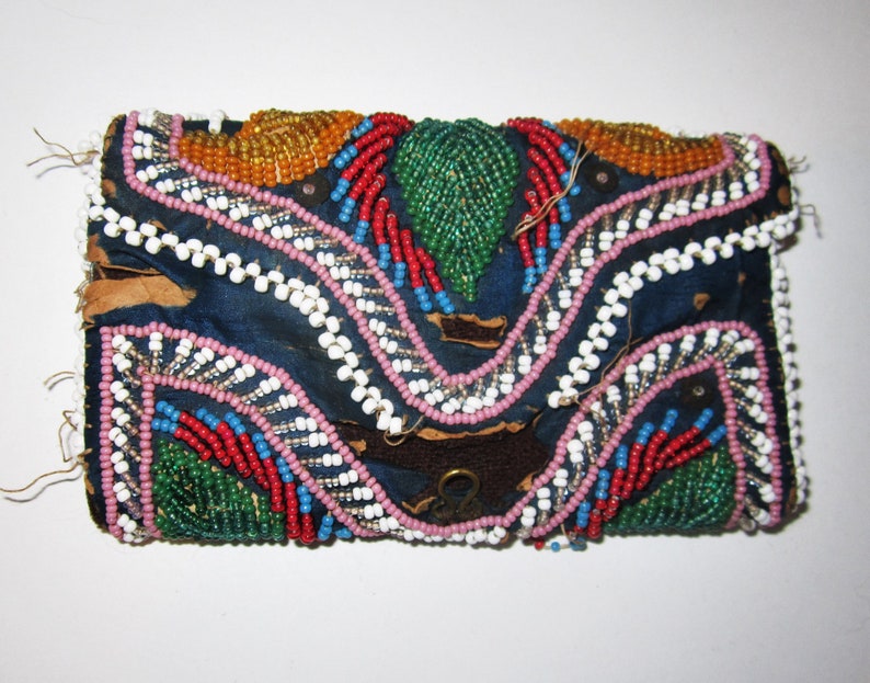 May include: A small, blue fabric pouch with a flap closure, decorated with colorful beads in a geometric pattern. The pouch has a metal clasp and is likely handmade.