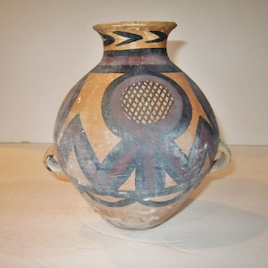 May include: A brown ceramic vase with two handles and a geometric design in black, white, and red. The vase has a round body and a narrow neck.