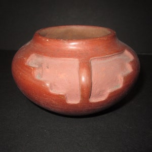 May include: A small, red clay pot with a geometric design. The pot is hand-crafted and has a rustic, earthy feel.