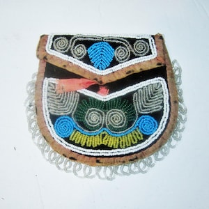 May include: A small, beaded pouch with a flap closure. The black background is decorated with blue, green, yellow, and white beads in a symmetrical pattern. The edges are trimmed with a beaded fringe. The flap is a light brown colour.