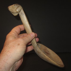 Puede incluir: Una cuchara de madera con un mango tallado en forma de cabeza de perro. La cuchara es de color marrón y tiene un acabado de madera natural.