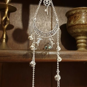 May include: Silver hanging ornament with a crescent moon design, two bunny charms, a key charm, and a Celtic knot charm. The ornament has multiple silver bells hanging from it.