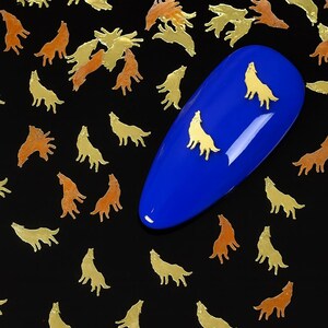Può includere: Decorazioni per nail art a forma di lupo dorate e color rame sparse su una superficie nera. Un'unghia blu a forma ovale presenta tre decorazioni a forma di lupo dorato. Le decorazioni sono piccole e dettagliate.
