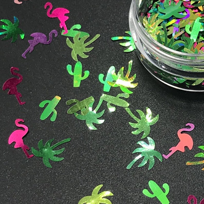 Op de afbeelding: Assortiment van iriserende groene, roze en paarse glittervormen, waaronder palmbomen, flamingo's en cactussen.
