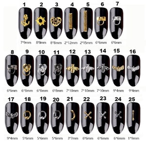 May include: A collection of 25 nail art charms in gold and silver tones, displayed on black nail polish. Designs include an anchor, sun, heart, bars, rings, bees, wings, crosses, and a curved line. Sizes vary from 1mm to 15mm.