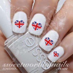 May include: Nail art decals featuring a red, white and blue heart-shaped Union Jack flag design. The decals are applied to white painted fingernails.
