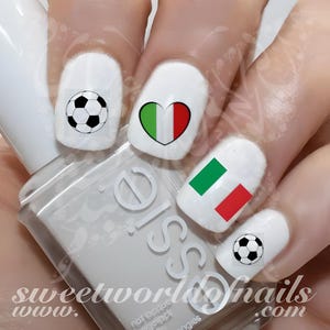 Puede incluir: Esmalte de uñas blanco con diseños de balón de fútbol y bandera italiana. Las uñas presentan un diseño de balón de fútbol, un corazón con la bandera italiana y la bandera italiana. La imagen también muestra el texto "sweetworldofnails.com".