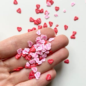 May include: A pile of pink and red heart-shaped sprinkles with the word "LOVE" printed on them.