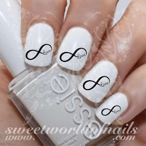 Peut inclure: Quatre ongles blancs avec des autocollants d'art d'ongles en forme de symbole d'infini noir. Chaque autocollant a le mot "Love" écrit à côté du symbole d'infini.