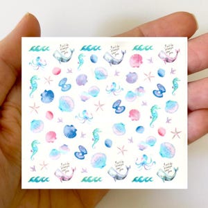 Può includere: Un foglio di adesivi ad acquerello colorati con motivi marini, tra cui balene, cavallucci marini, conchiglie, stelle marine e un polpo. Gli adesivi includono anche il testo "I will be always love you" ripetuto più volte.