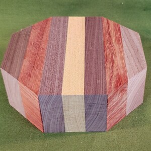 May include: An octagonal wooden bowl crafted from various wood types, showcasing a spectrum of colors from light beige to deep reds and purples. The bowl's design highlights the natural grain and textures of the wood.