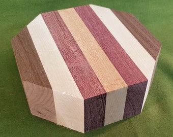 May include: Octagonal wooden serving board with alternating stripes of light and dark wood. The board is made of maple, walnut, and purpleheart wood.