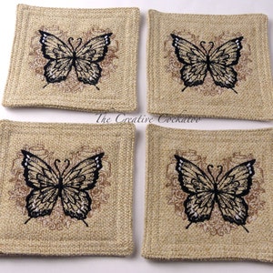 May include: Set of four square beige coasters with a black butterfly design. Each coaster features a brown floral pattern surrounding the butterfly.