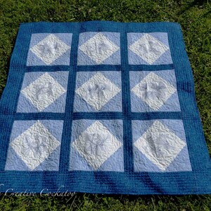 May include: A blue and white quilt with a diamond pattern. The quilt is made of squares with a white background and a blue diamond in the center. The diamonds have a floral design in white.