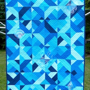 May include: A blue and white quilt with a geometric pattern. The quilt features white embroidered images of seashells and an octopus. The quilt is hanging on a clothesline.