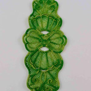 May include: Green lace trim with a scalloped design. The lace is a delicate, intricate pattern with a slightly ombre effect.