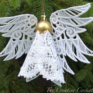 May include: White lace angel ornament with gold ball and intricate details, hanging on a green Christmas tree.