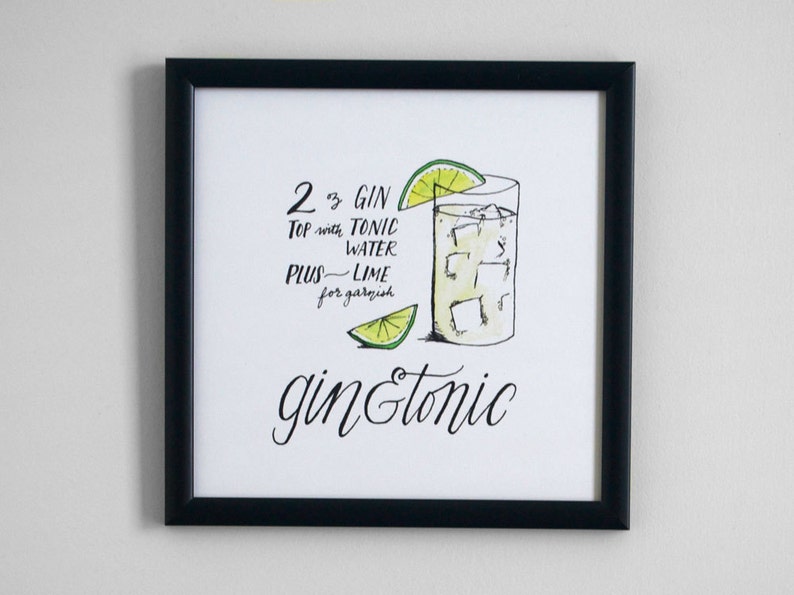 May include: A framed print with a black border featuring a watercolor illustration of a gin and tonic. The image includes a glass of the cocktail with ice and a lime wedge, along with the recipe: "2 oz Gin, Top with Tonic Water, Plus Lime for garnish."